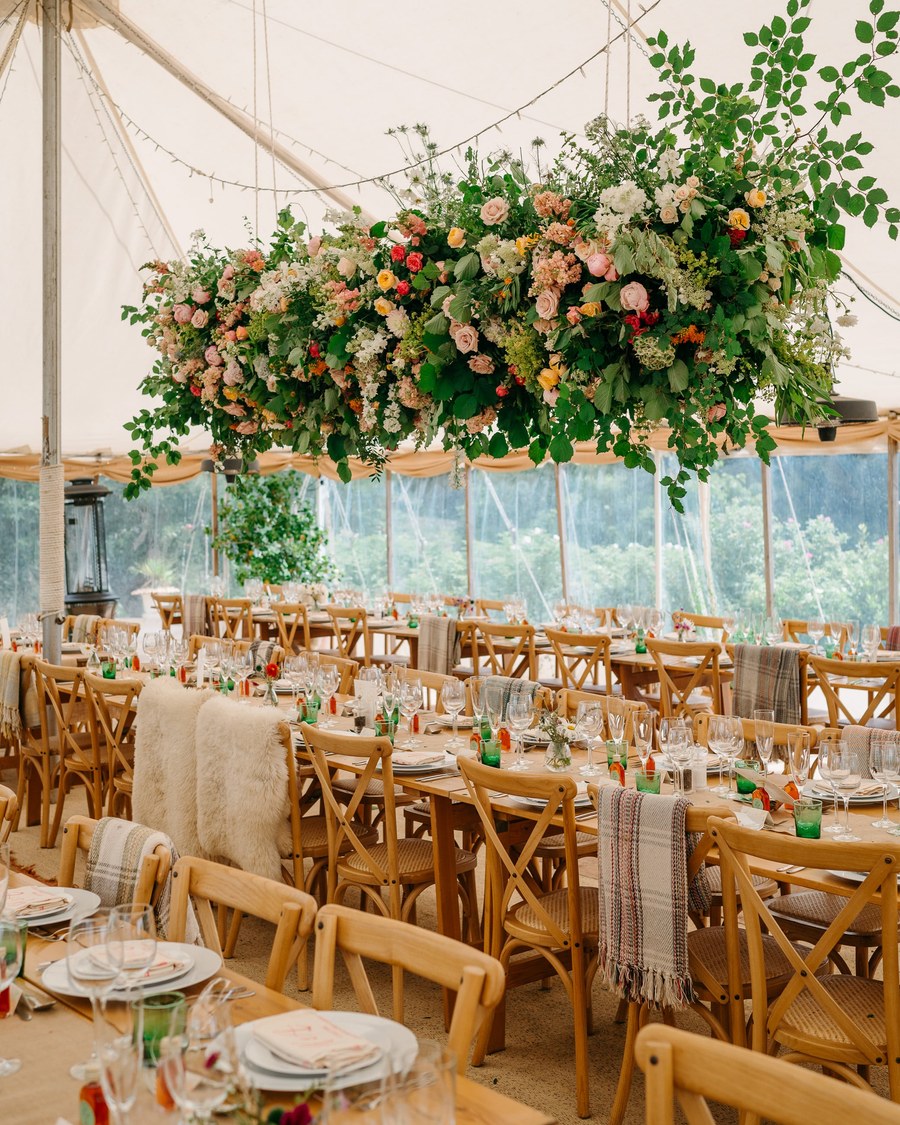 A marquee interior is set with long wooden banquet tables, cross-back chairs, and woven place mats