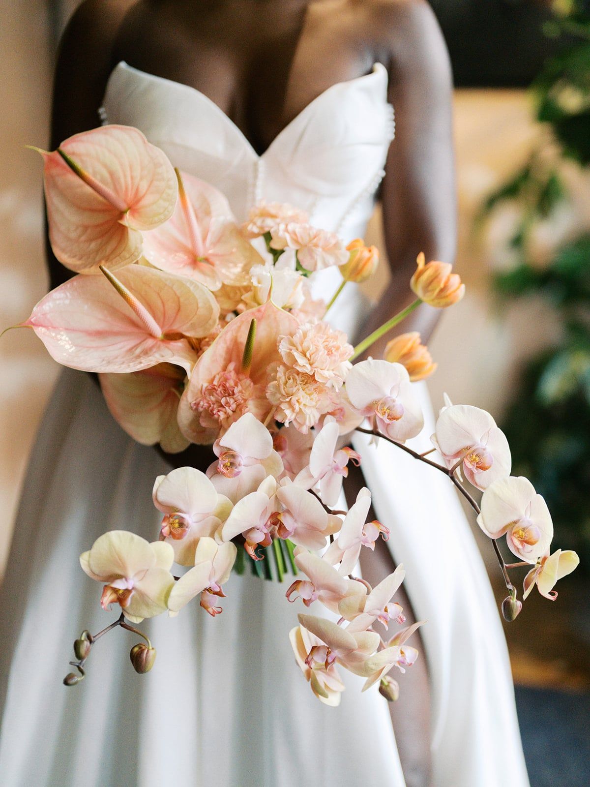 A bride holds an elongated, cascading bouquet featuring pale peach anthuriums, peachy-pink
