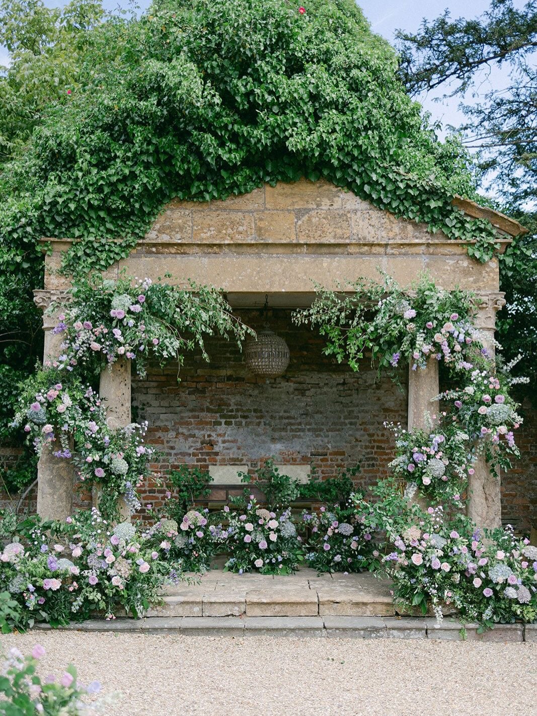 An outdoor stone folly adorned with lush floral arrangements in soft pastels, set up for a wedding