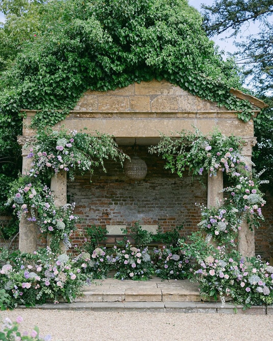 An outdoor stone folly adorned with lush floral arrangements in soft pastels, set up for a wedding