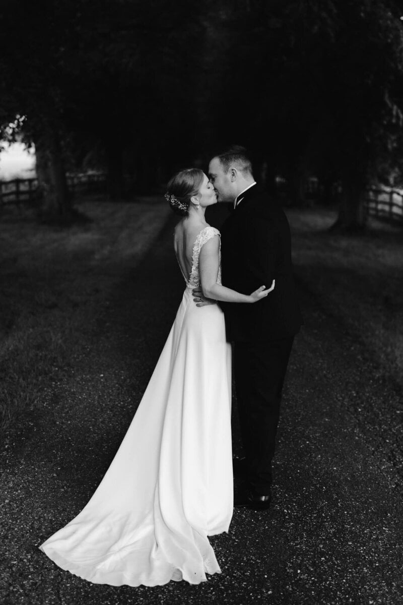 A bride in a white gown with an illusion lace back and a groom in a black suit share a tender kiss