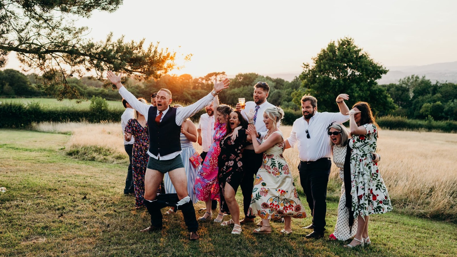 A group of wedding guests, including one man with his trousers around his ankles revealing striped