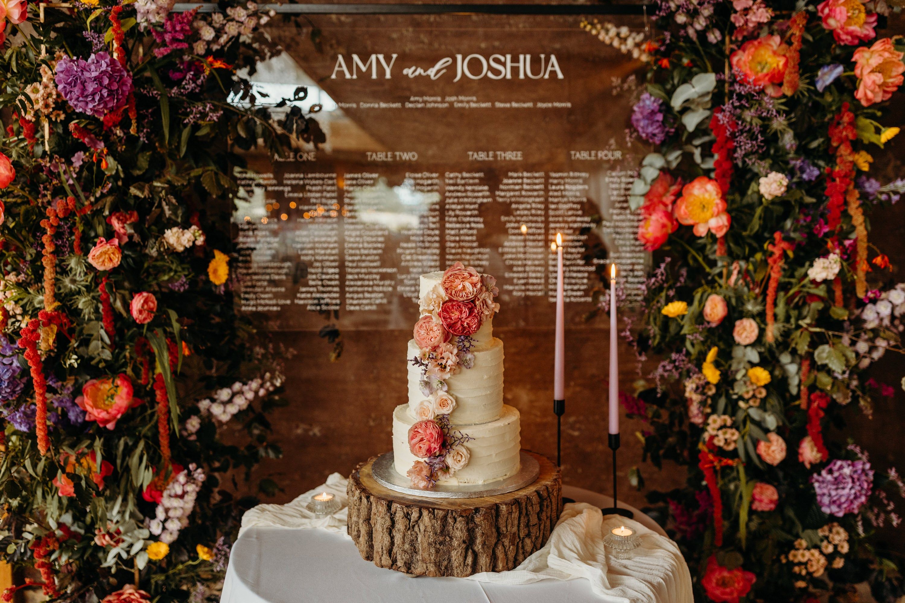 A wedding cake display features a three-tier buttercream cake decorated with peach-toned garden