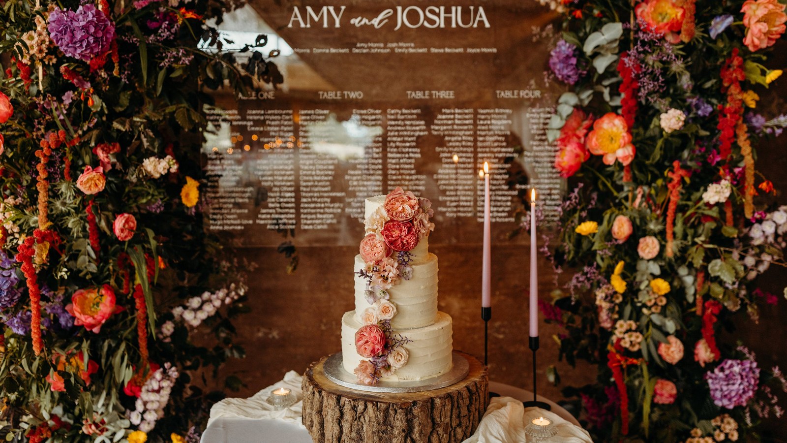 A wedding cake display features a three-tier buttercream cake decorated with peach-toned garden