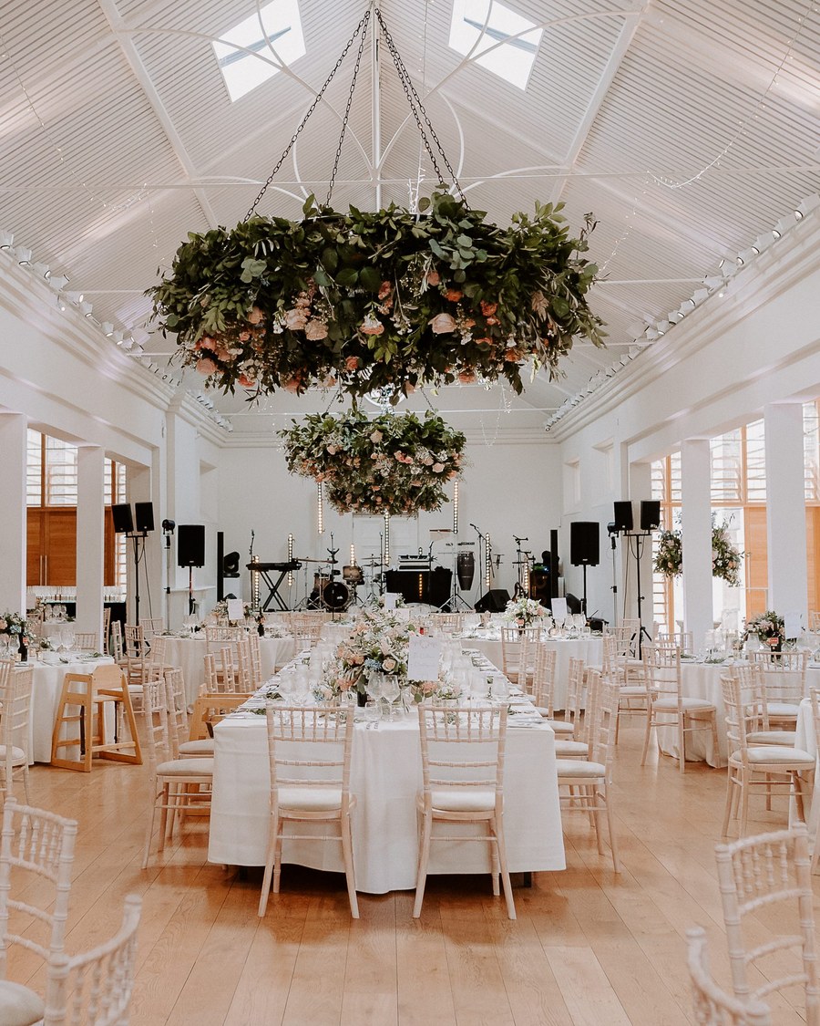 A wide shot of a wedding reception set up in a bright, modern hall with high white ceilings and