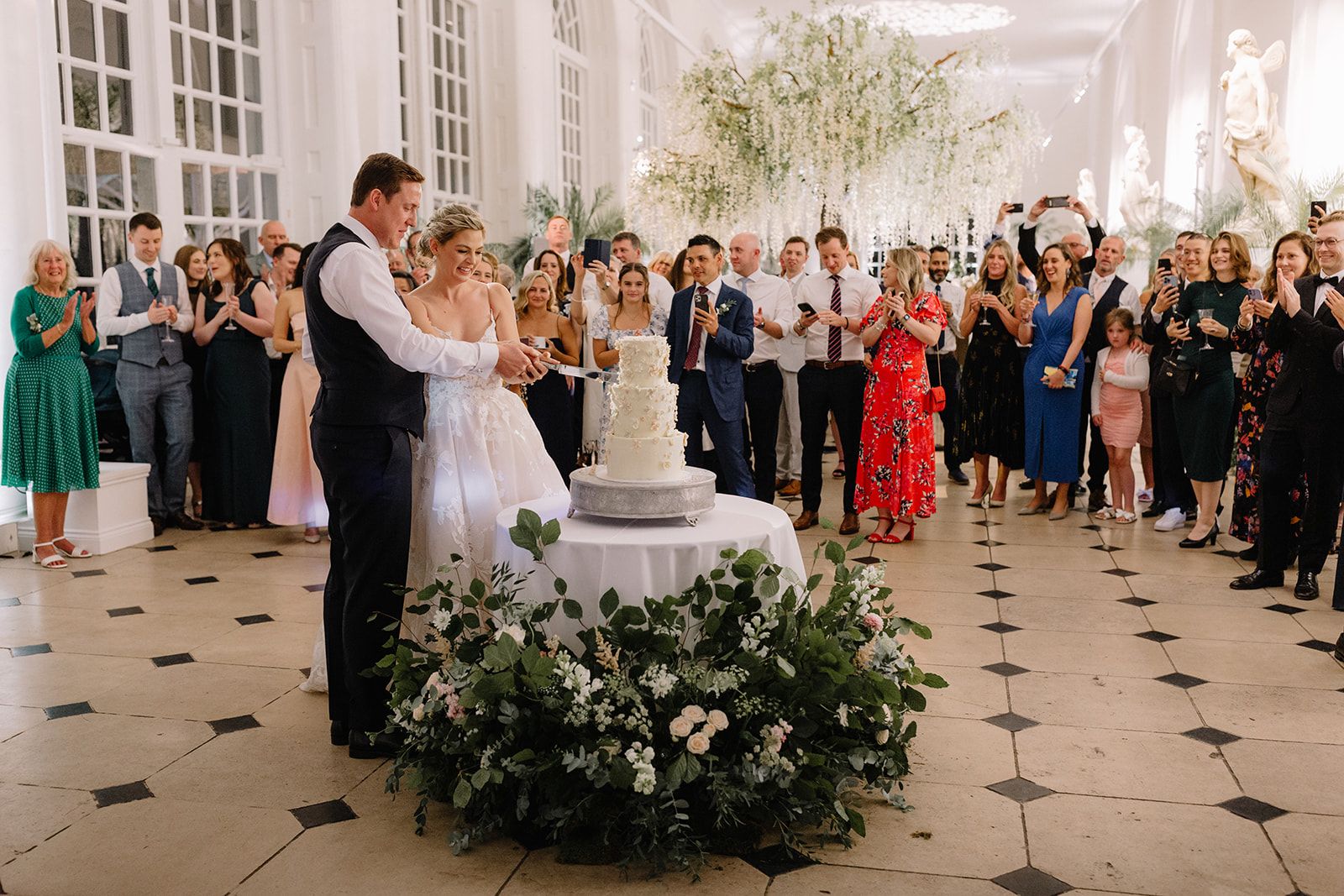 A three-tier round cake with a smooth white finish, adorned with delicate white and blush flowers