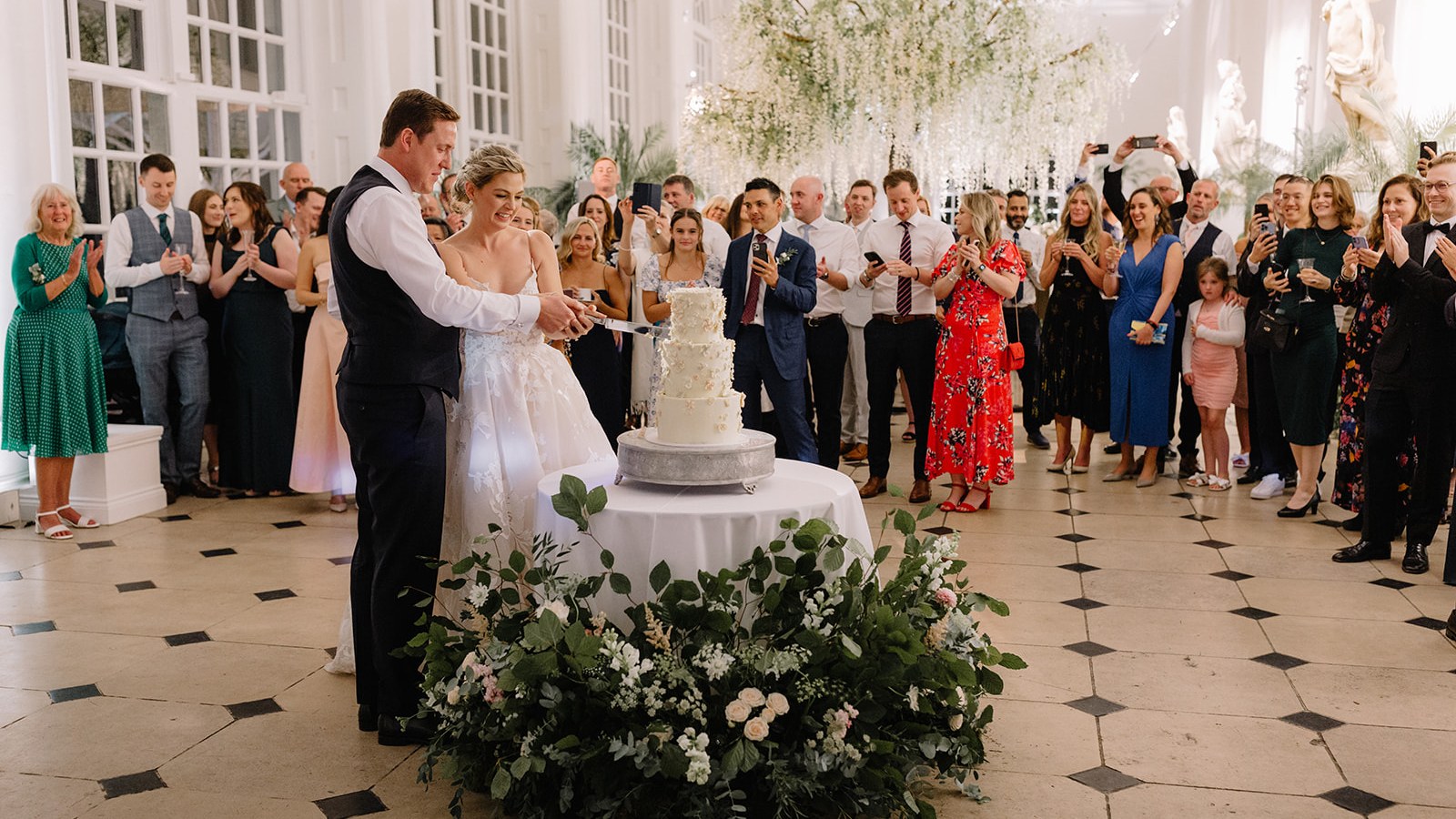 A three-tier round cake with a smooth white finish, adorned with delicate white and blush flowers