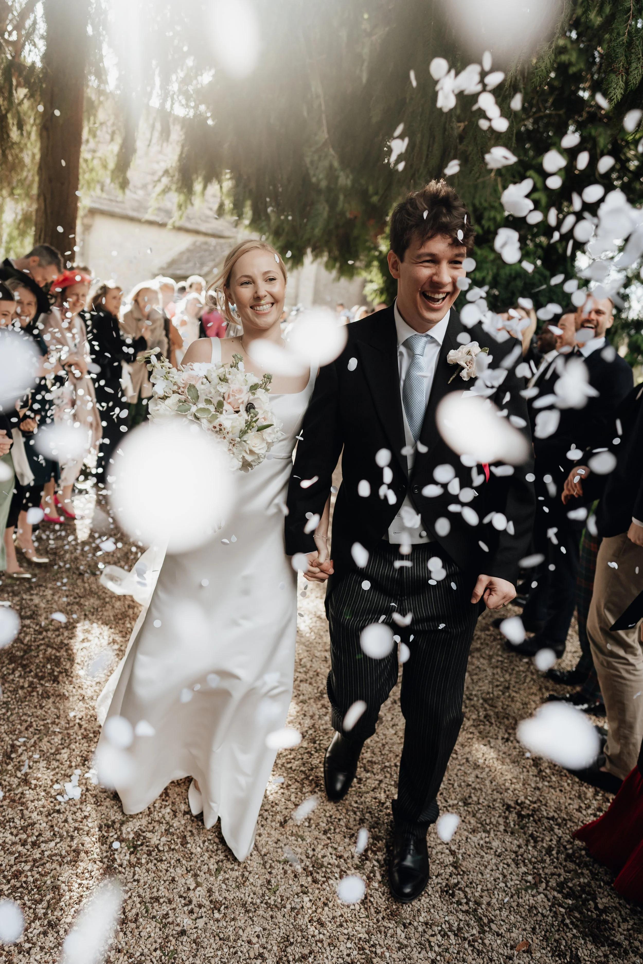 The newly married couple walks hand-in-hand down a gravel path, smiling and laughing as white