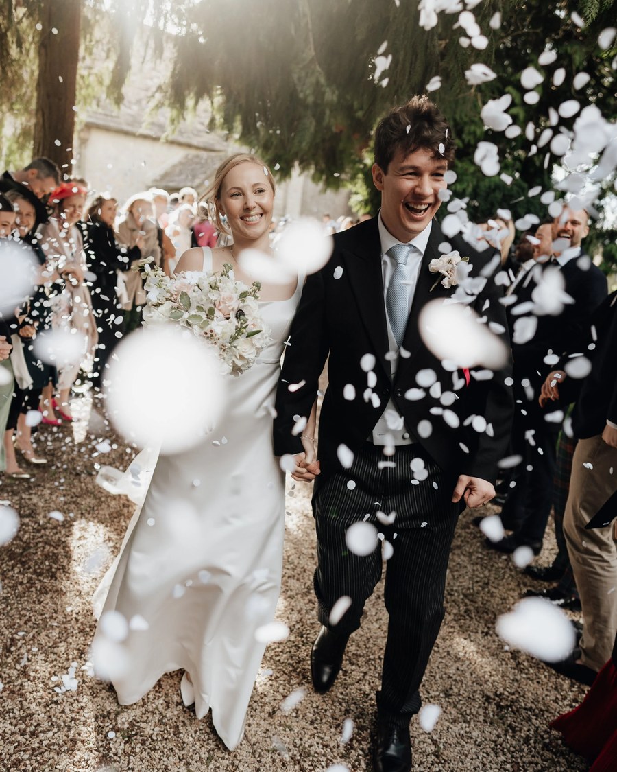 The newly married couple walks hand-in-hand down a gravel path, smiling and laughing as white
