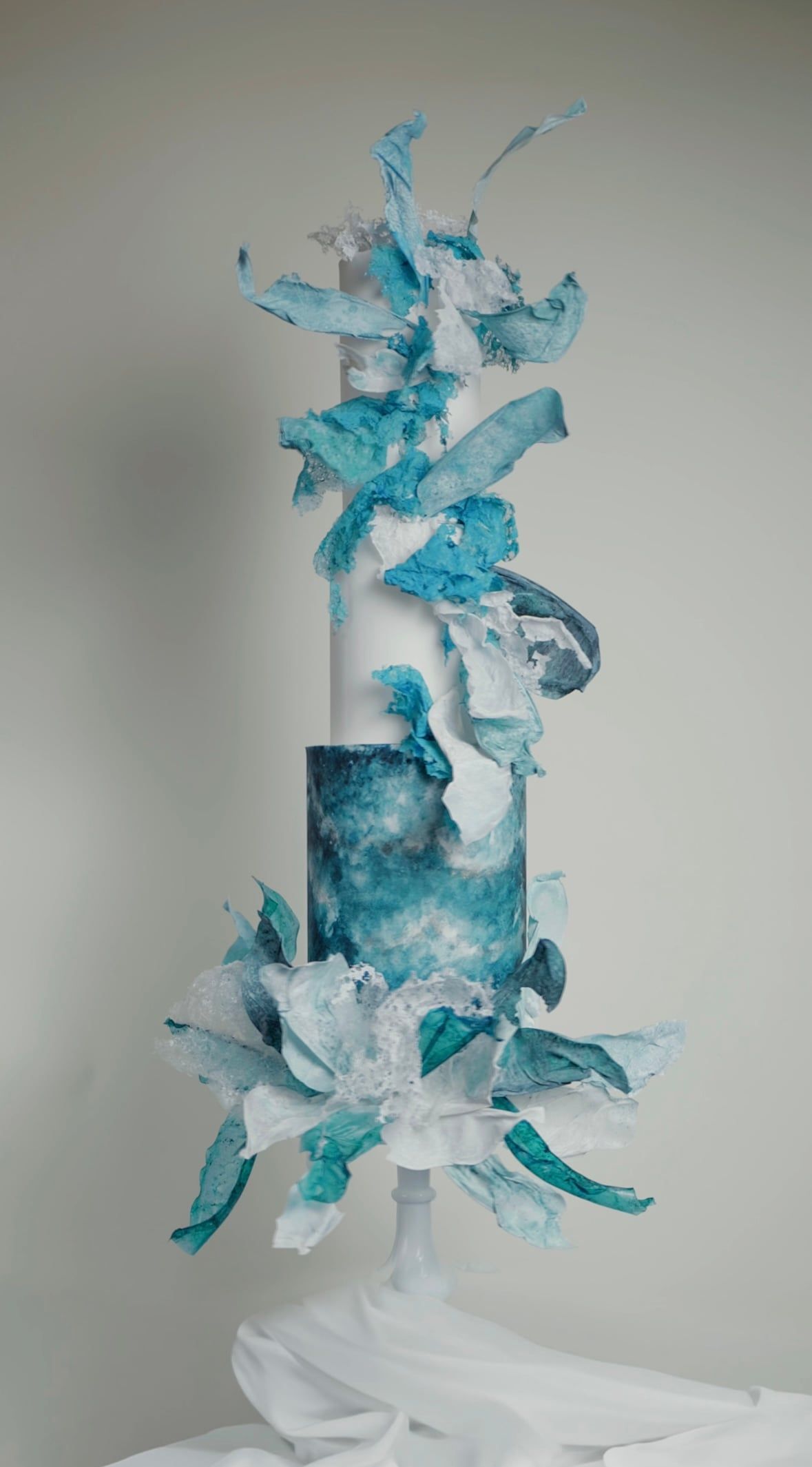 A three-tier round cake featuring a lower tier with a hand-painted blue and turquoise watercolour