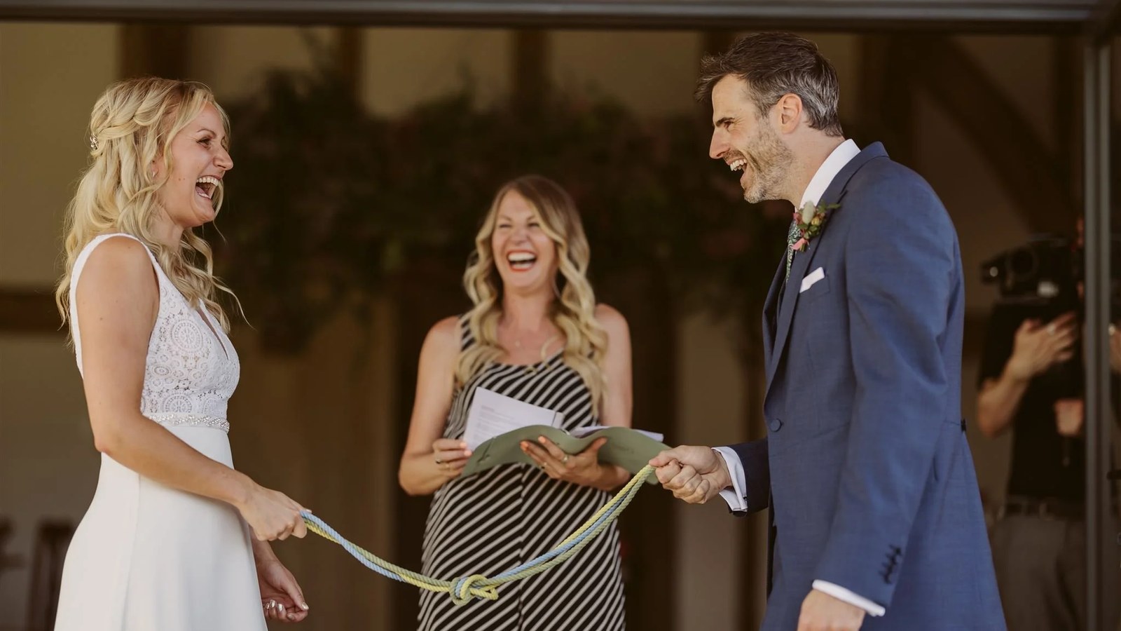 A close-up of a celebrant, couple, and a handfasting cord, captured during a ceremony. All three