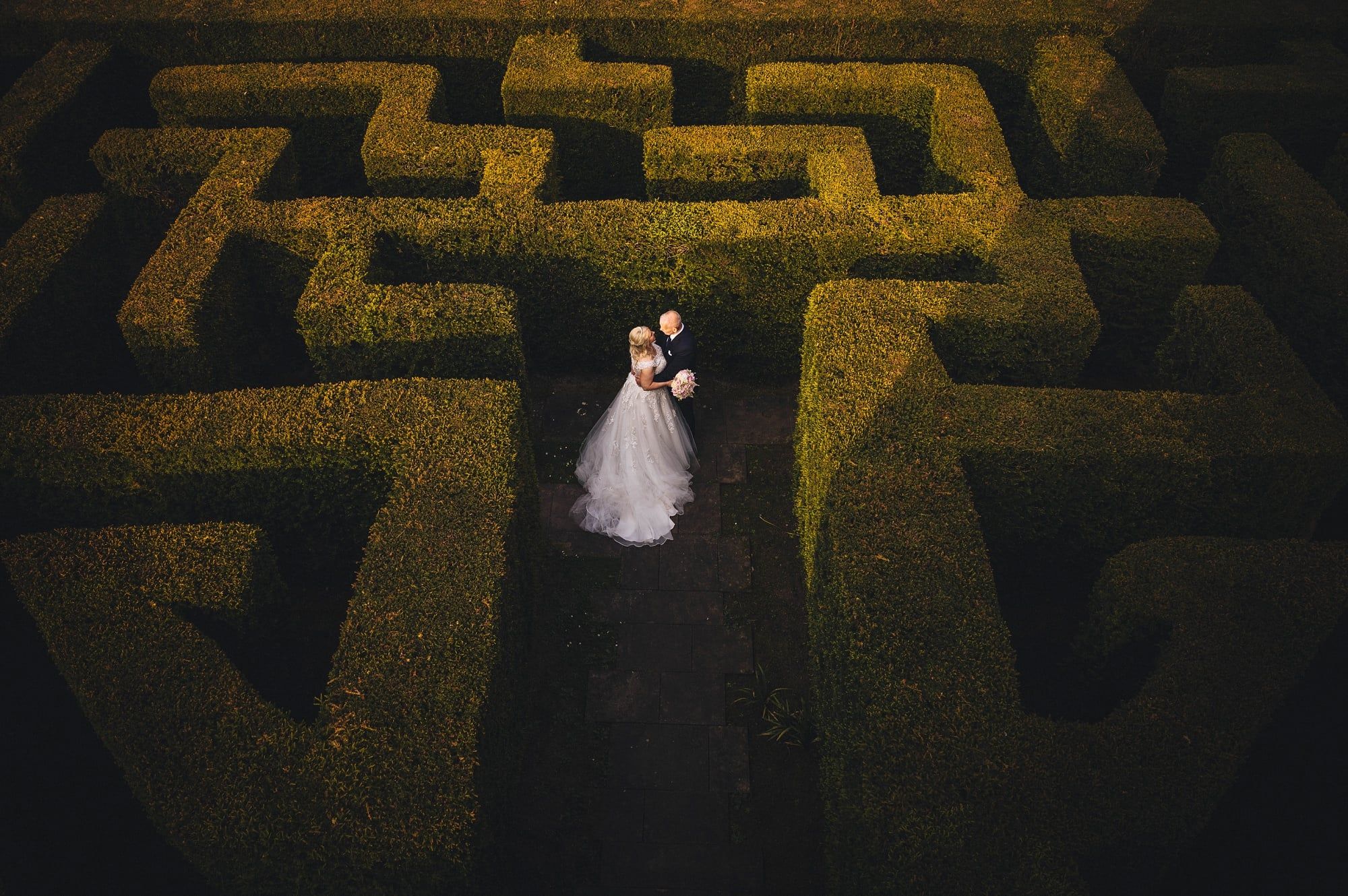 A bride in a white embellished gown and a groom in a dark suit stand intimately amidst the tall