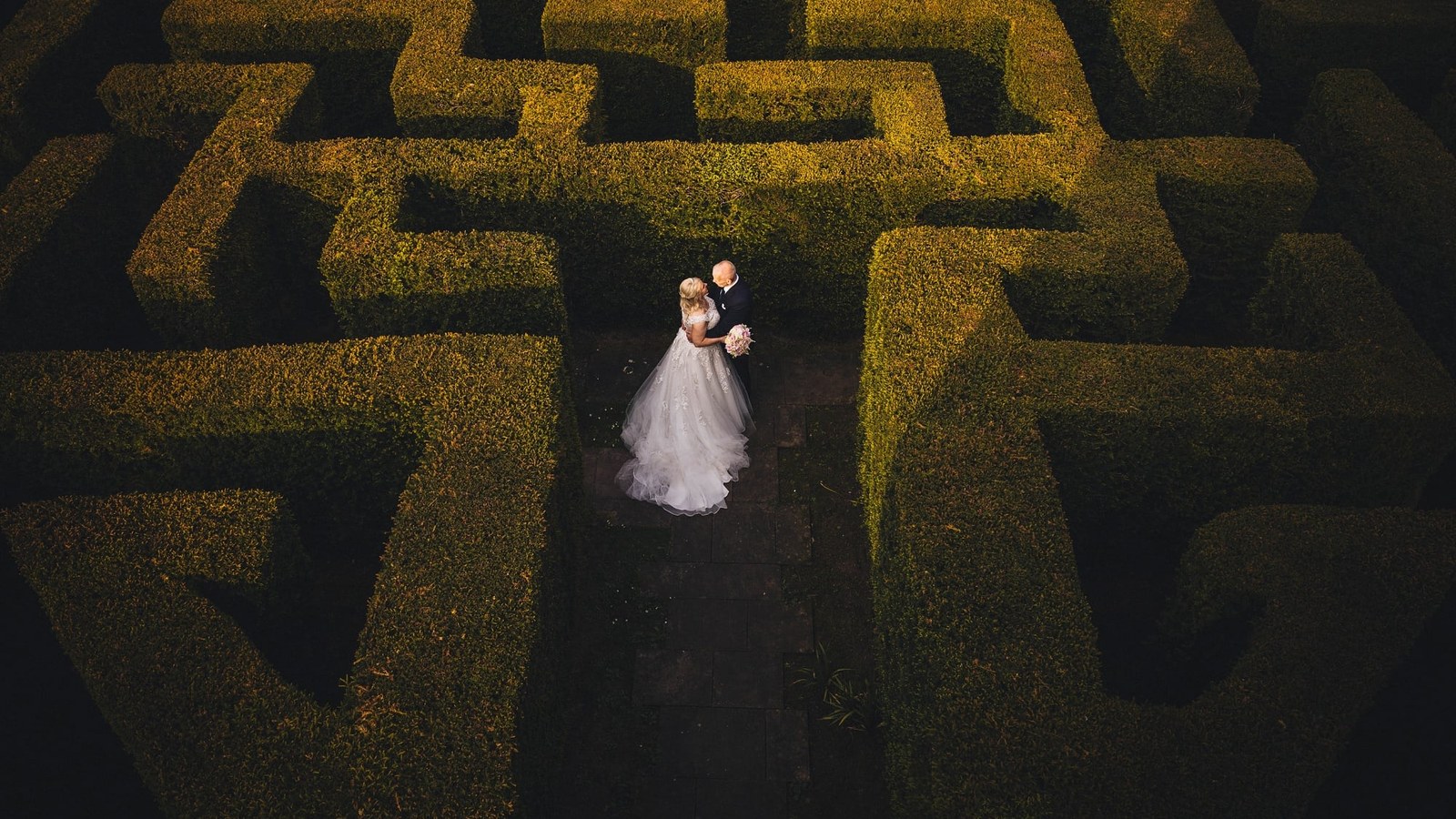 A bride in a white embellished gown and a groom in a dark suit stand intimately amidst the tall