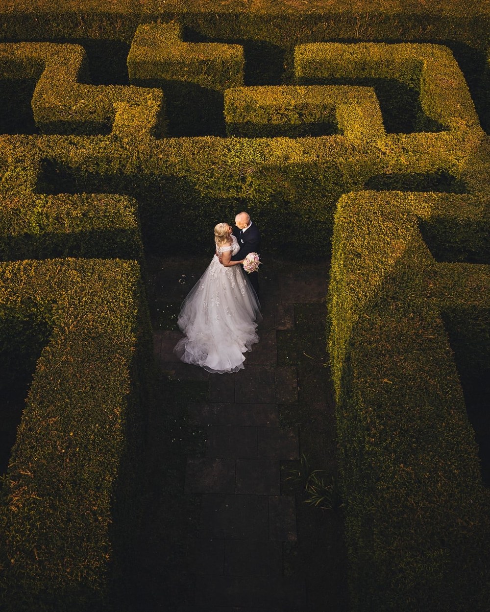 A bride in a white embellished gown and a groom in a dark suit stand intimately amidst the tall
