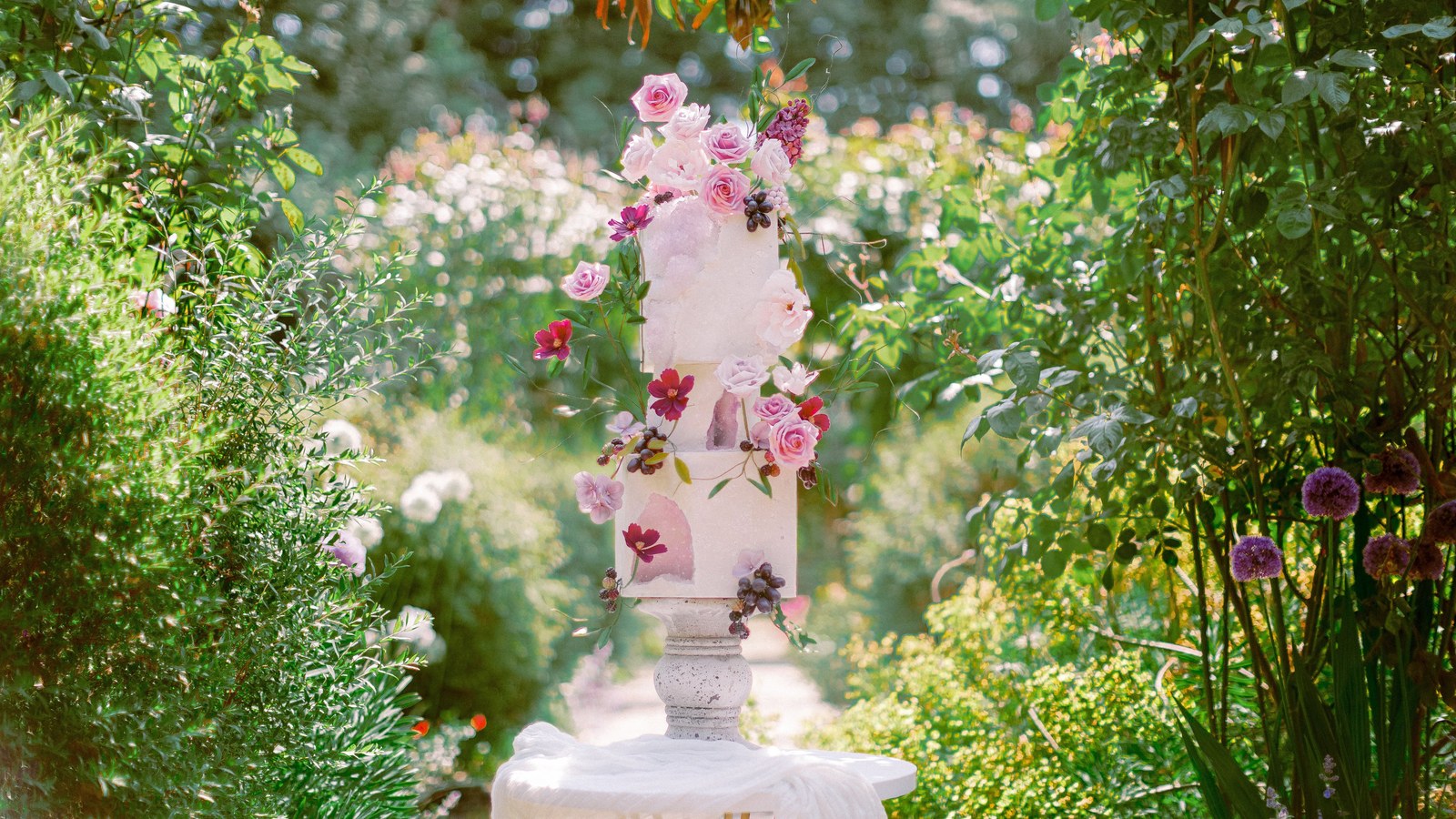 A three-tier, square cake with an off-white, slightly textured surface, possibly semi-naked or