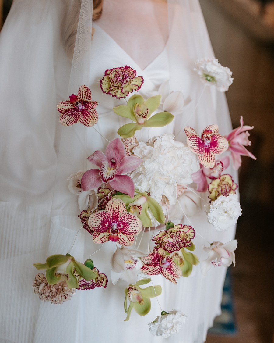 A close-up of a bride holding a contemporary deconstructed bouquet featuring individual blooms of