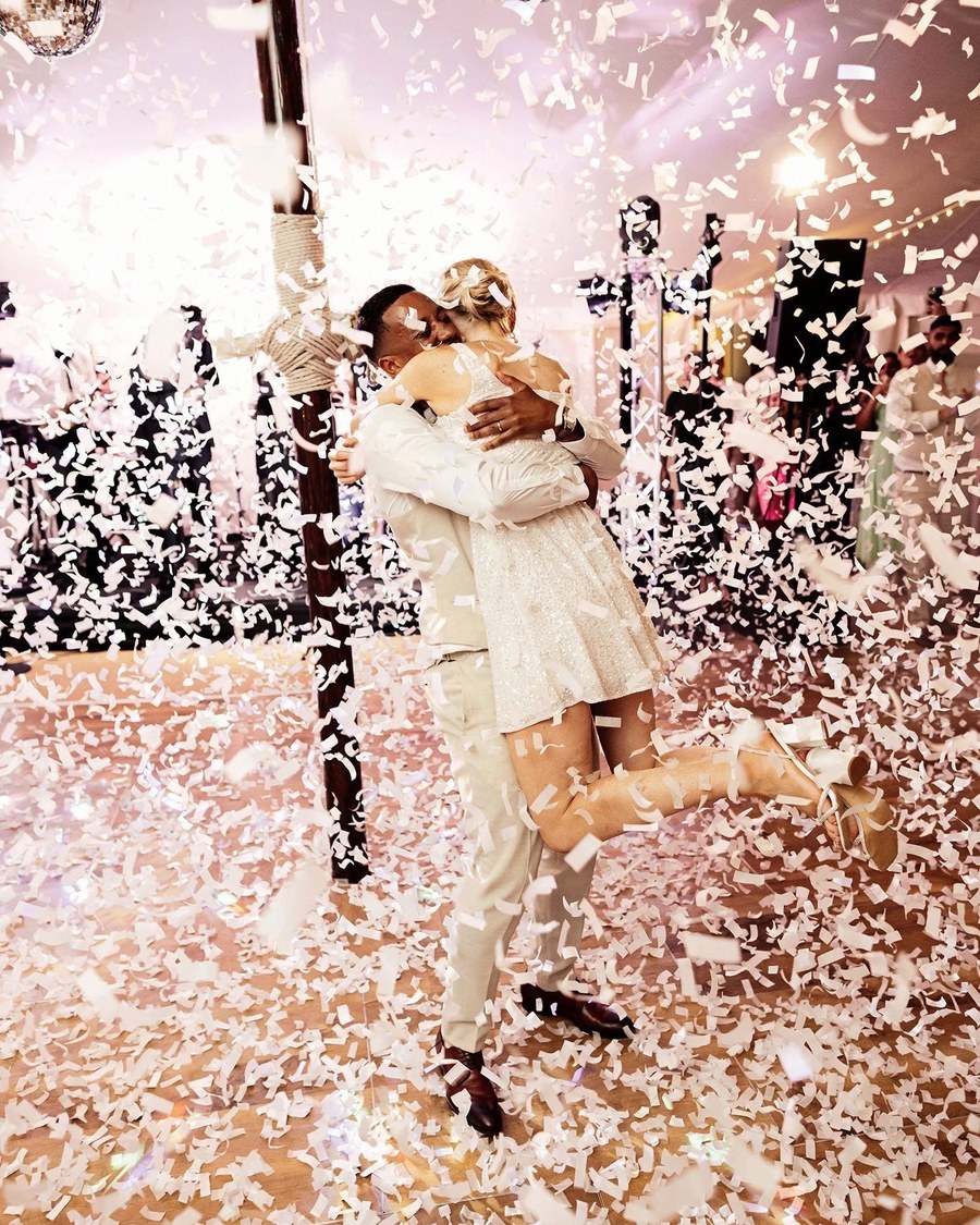 A couple embraces tightly on a wooden dance floor, surrounded by white falling confetti and disco