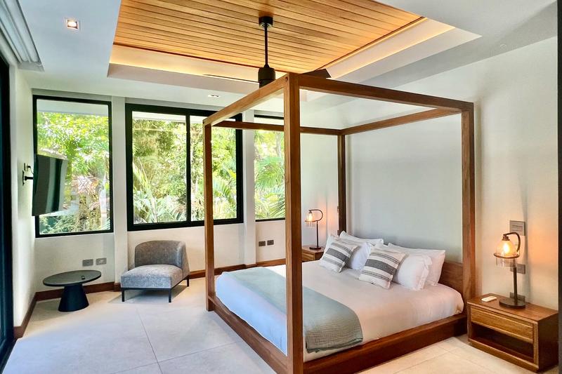 Canopy bed beneath a wood ceiling with jungle view windows at Villa de Grace