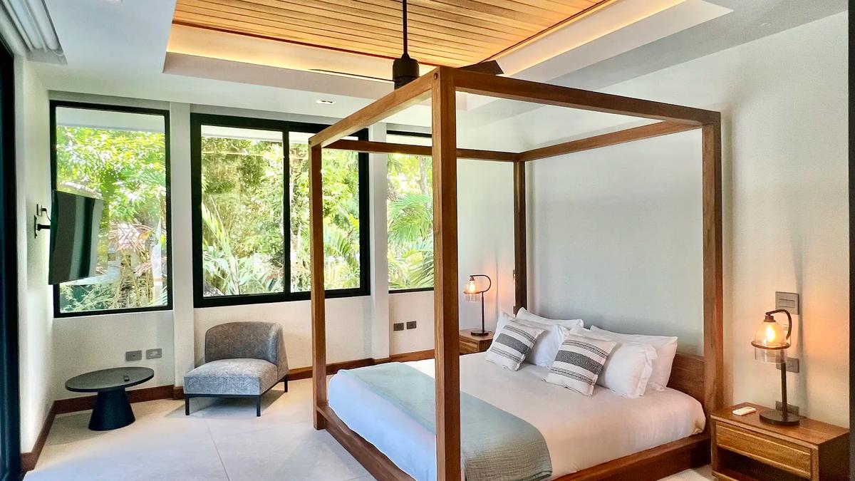 Canopy bed beneath a wood ceiling with jungle view windows at Villa de Grace