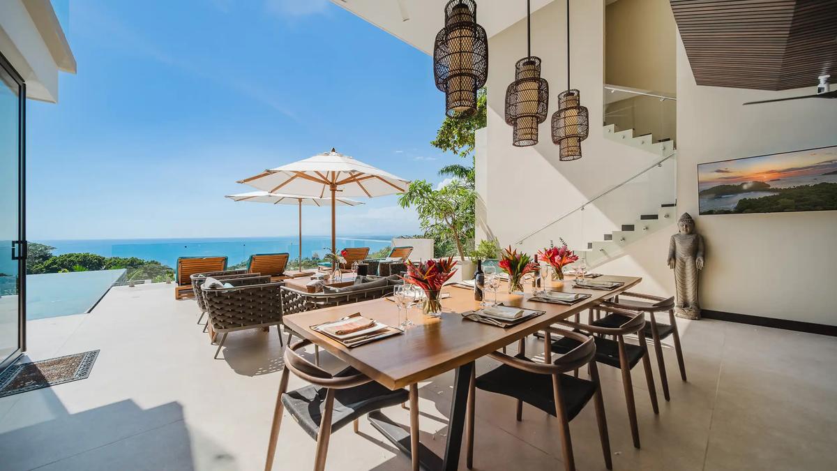 Covered terrace dining at Casa Nola with wicker lanterns, Buddha statue, and ocean horizon