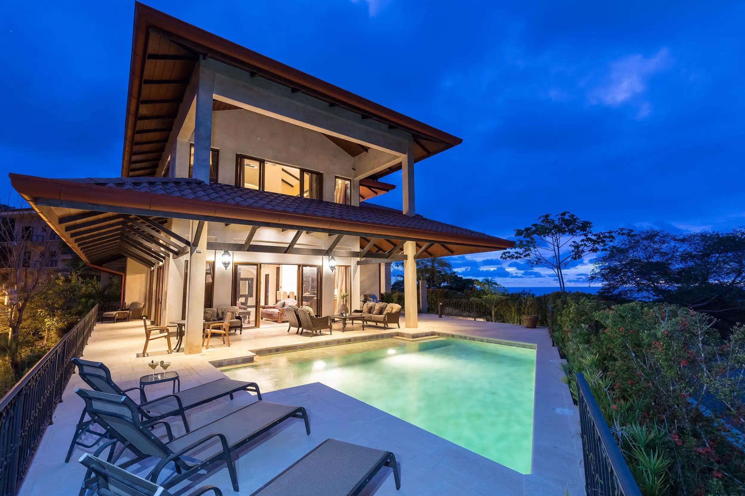 Villa Marbella at dusk with lit pool, lounge chairs, and ocean horizon
