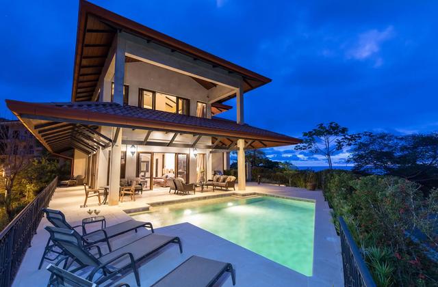 Villa Marbella at dusk with lit pool, lounge chairs, and ocean horizon