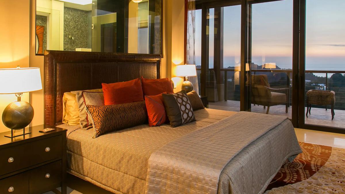 King bed with tiger-stripe and red pillows at Villa Celaje, sunset balcony beyond