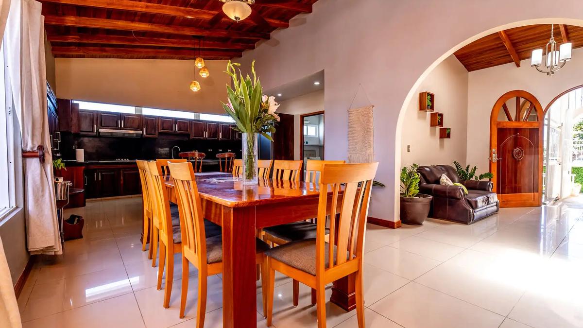 Long wooden dining table seating ten with open kitchen behind at Casa Alta Vista
