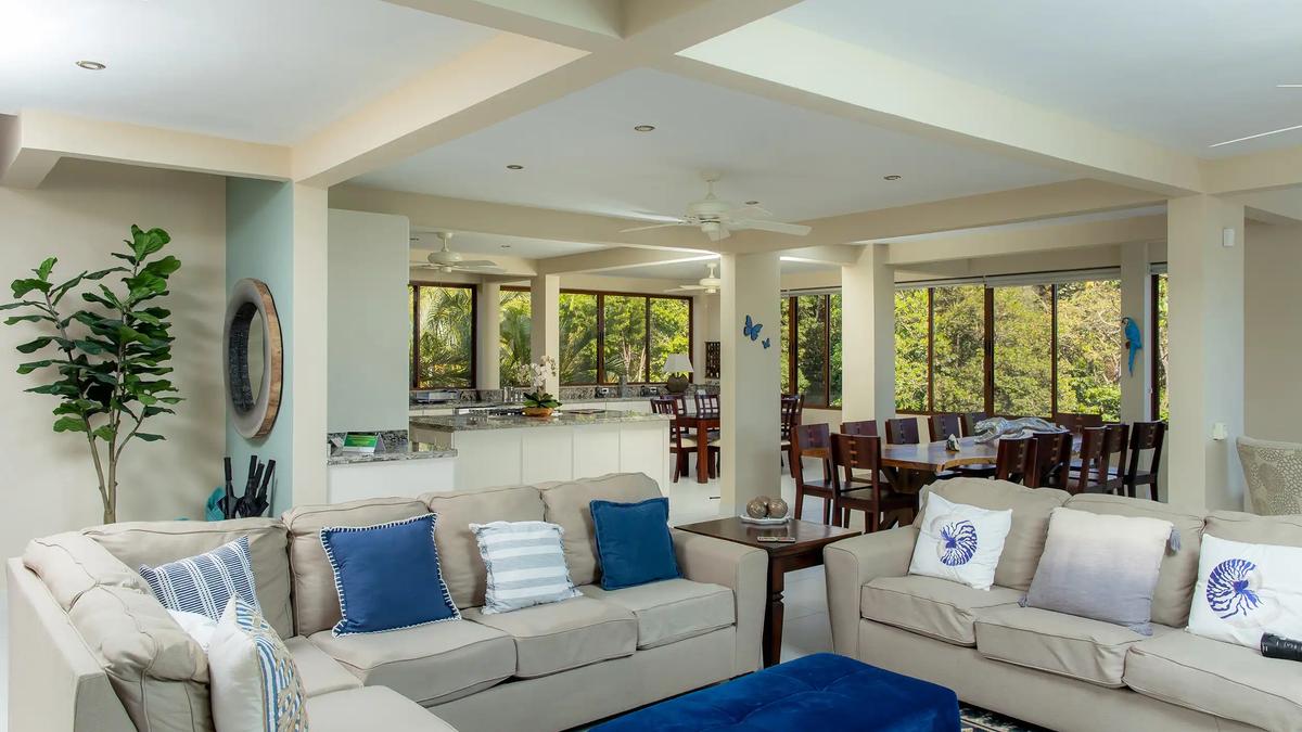 Open living area at Casa Mariposa with beige sofas, blue accents, and jungle windows