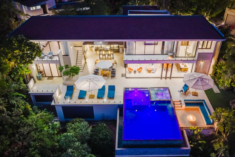 Night aerial of Casa Nola, the infinity pool lit blue among the trees