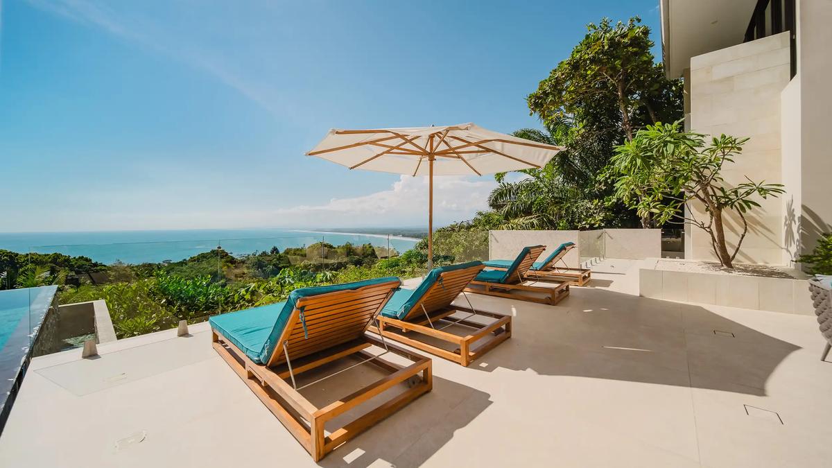 Teak loungers and umbrella on the Casa Nola pool deck overlooking the shoreline