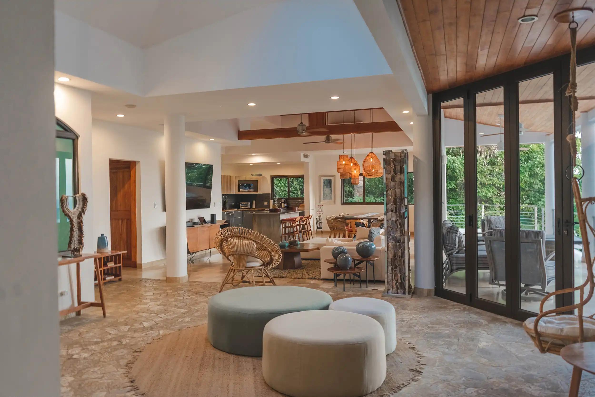 Open-plan lounge at Casa Anjali with rattan chair, poufs, and kitchen beyond