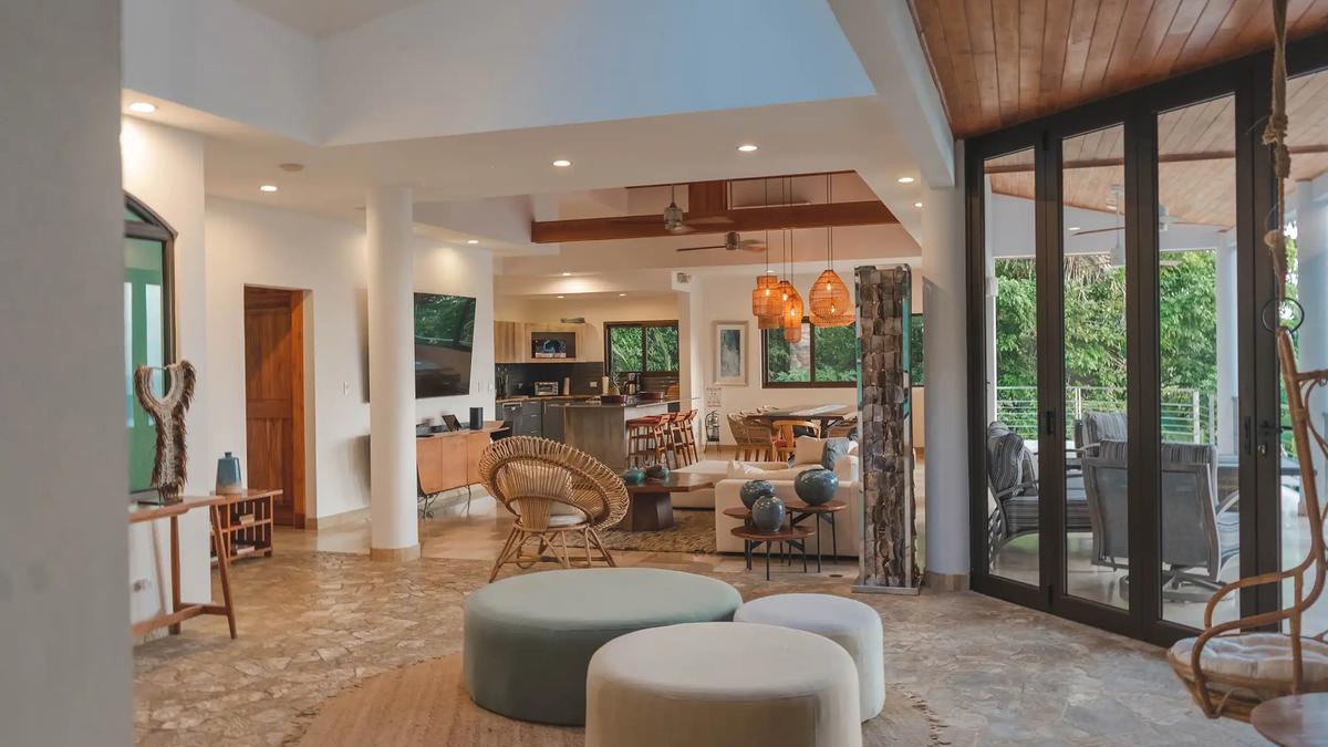 Open-plan lounge at Casa Anjali with rattan chair, poufs, and kitchen beyond