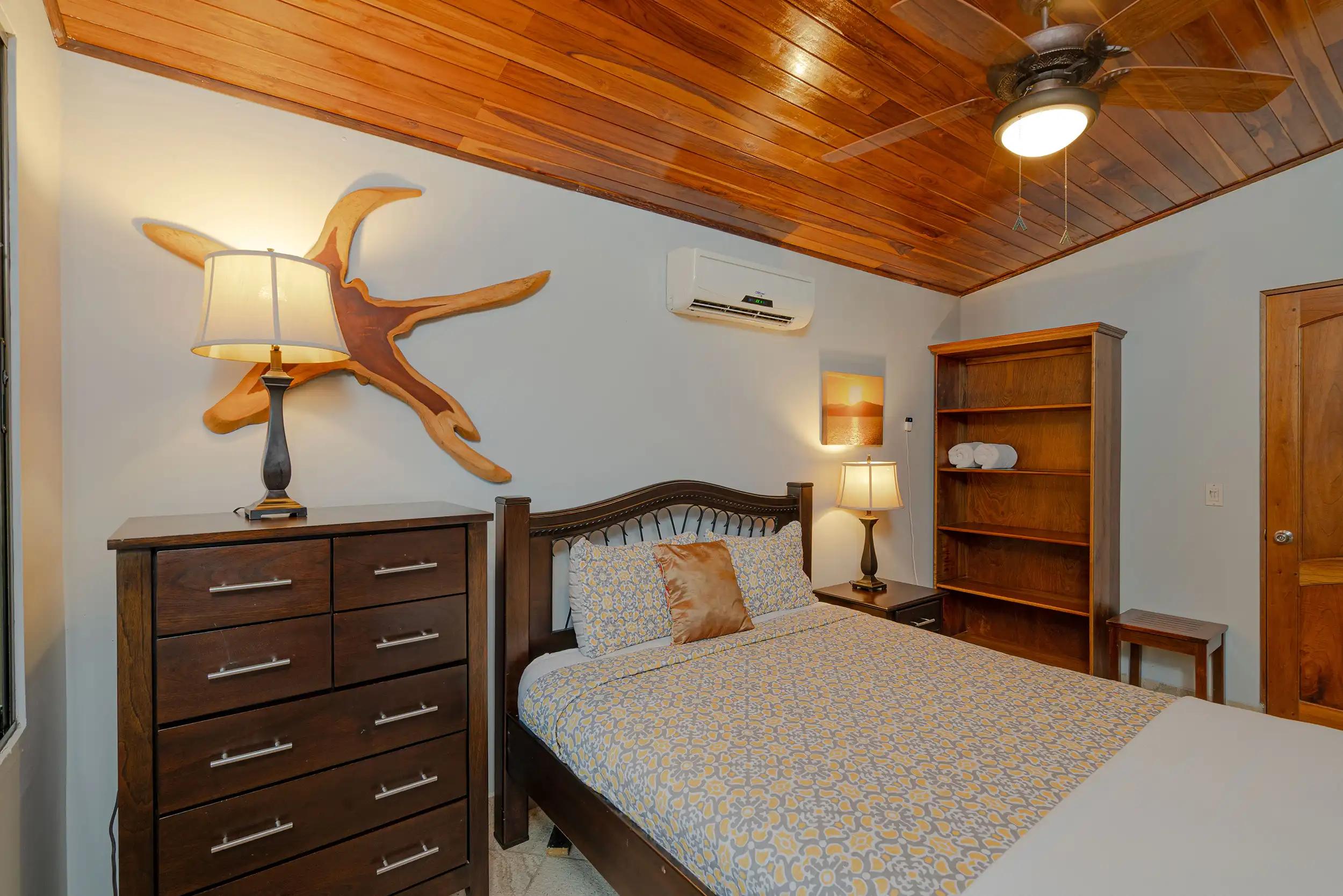 Casa Serenidad guest bedroom with dresser, ceiling fan, and driftwood art above the bed