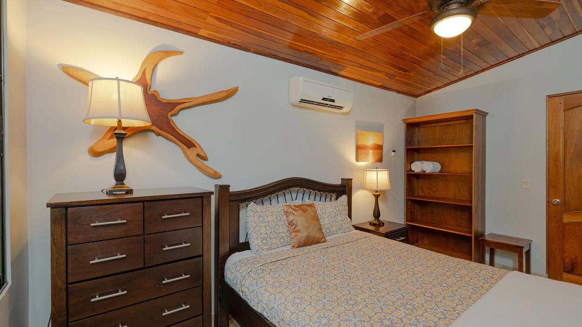 Casa Serenidad guest bedroom with dresser, ceiling fan, and driftwood art above the bed
