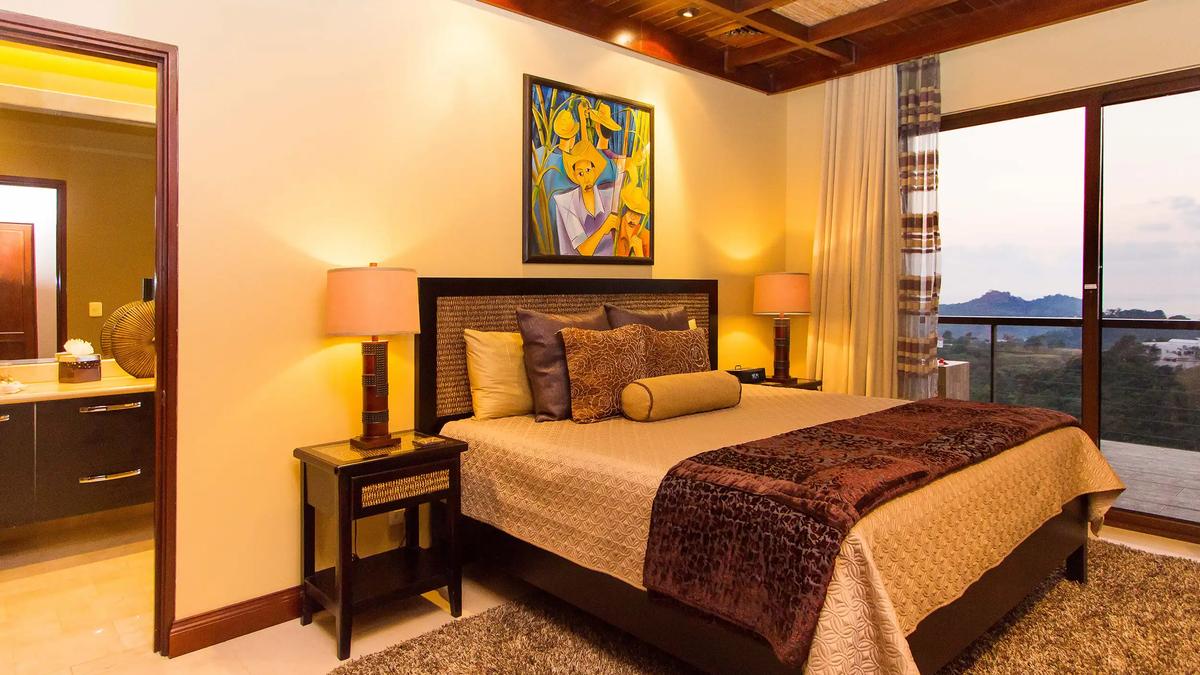 Bedroom at Villa Celaje with woven headboard, en suite bathroom, and balcony ocean view