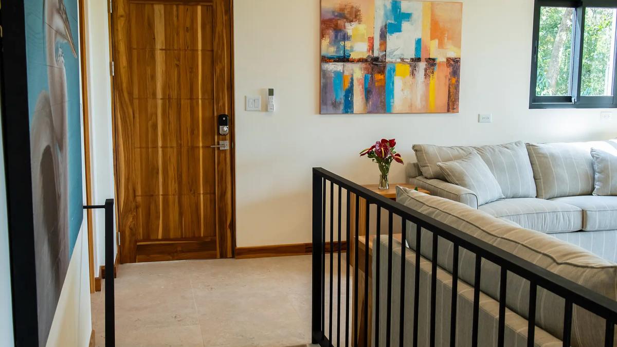 Stair landing at Casa Rambutan with striped sofa, abstract painting, and teak front door
