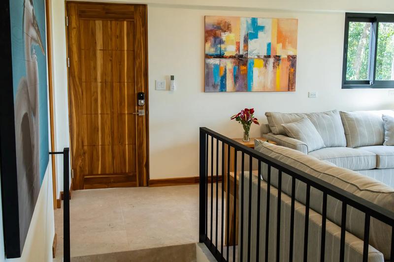 Stair landing at Casa Rambutan with striped sofa, abstract painting, and teak front door