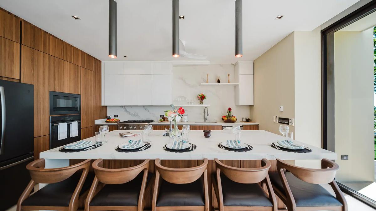 Kitchen island dining at Casa Nola with wood chairs, pendant lights, and black appliances