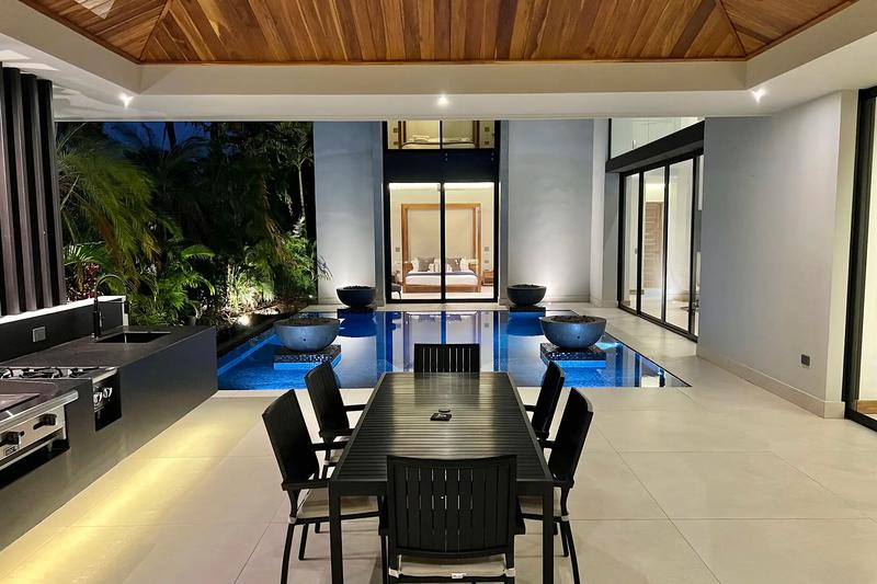 Outdoor dining table beside the lit pool and kitchen at Villa de Grace