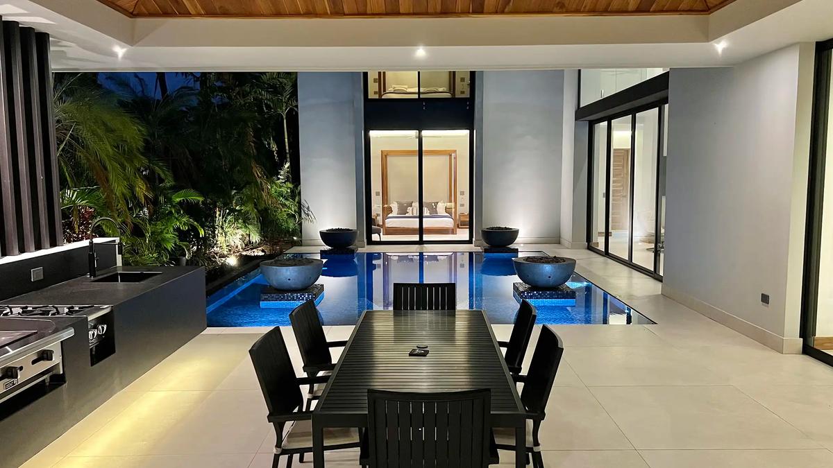 Outdoor dining table beside the lit pool and kitchen at Villa de Grace