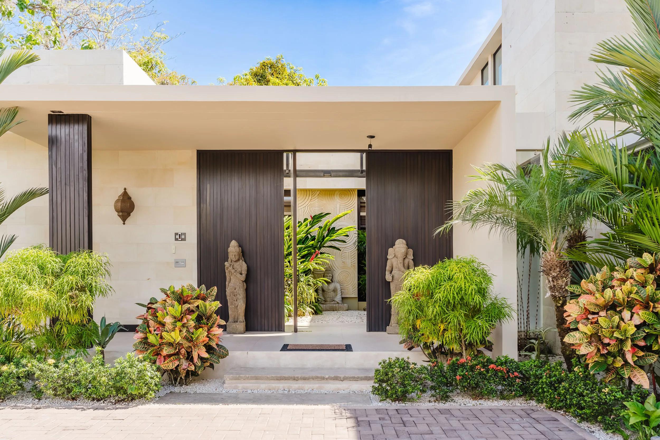 Entrance to Casa Nola with stone guardians, tropical planting, and a dark timber door