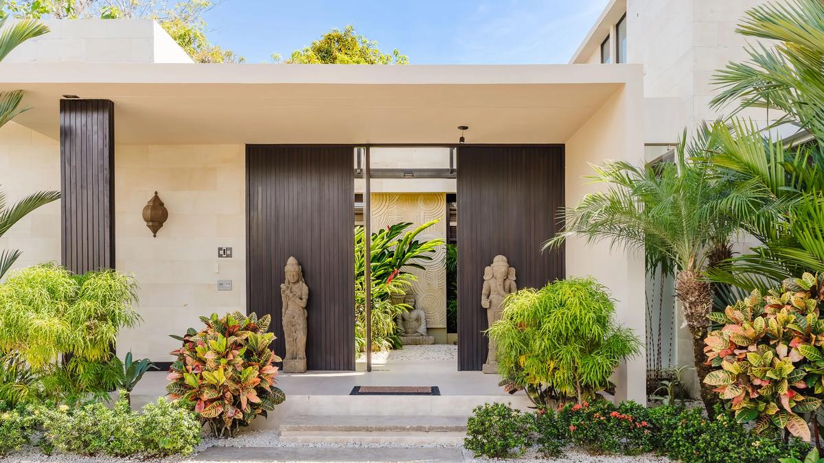 Entrance to Casa Nola with stone guardians, tropical planting, and a dark timber door