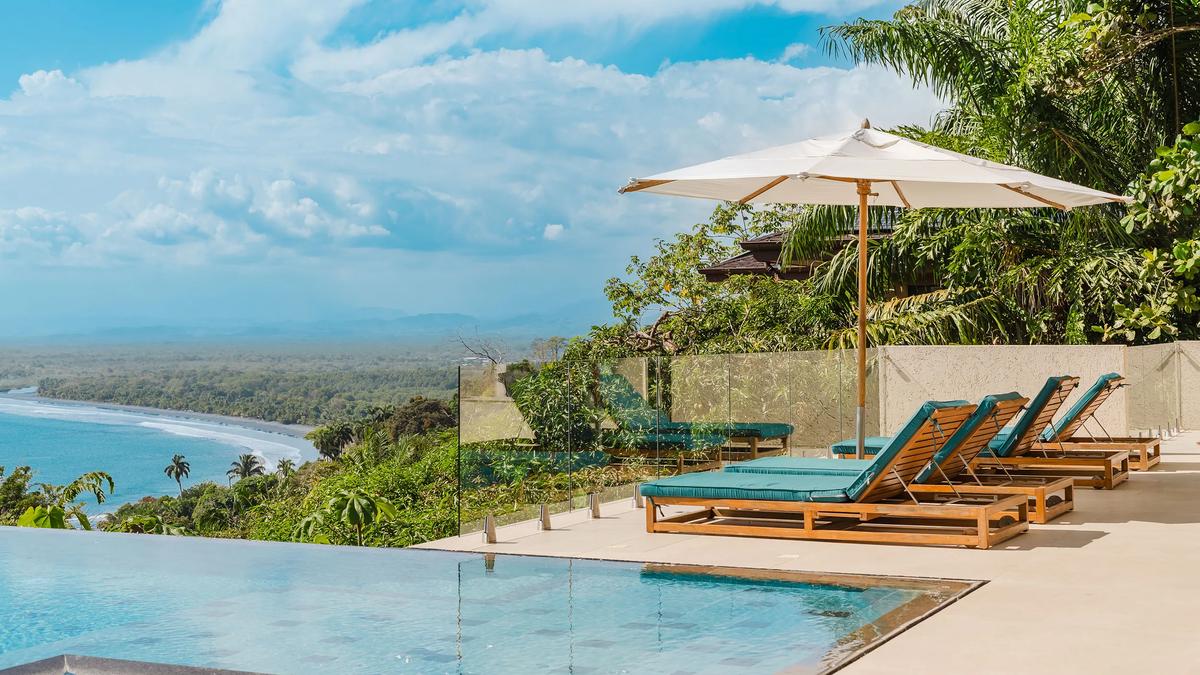 Infinity pool, loungers, and umbrella at Casa Nola with the coastline below