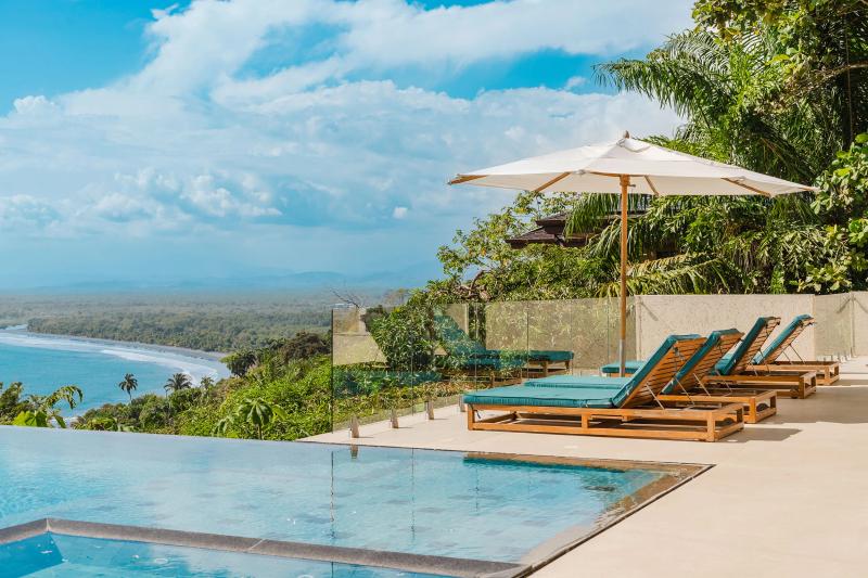 Infinity pool, loungers, and umbrella at Casa Nola with the coastline below