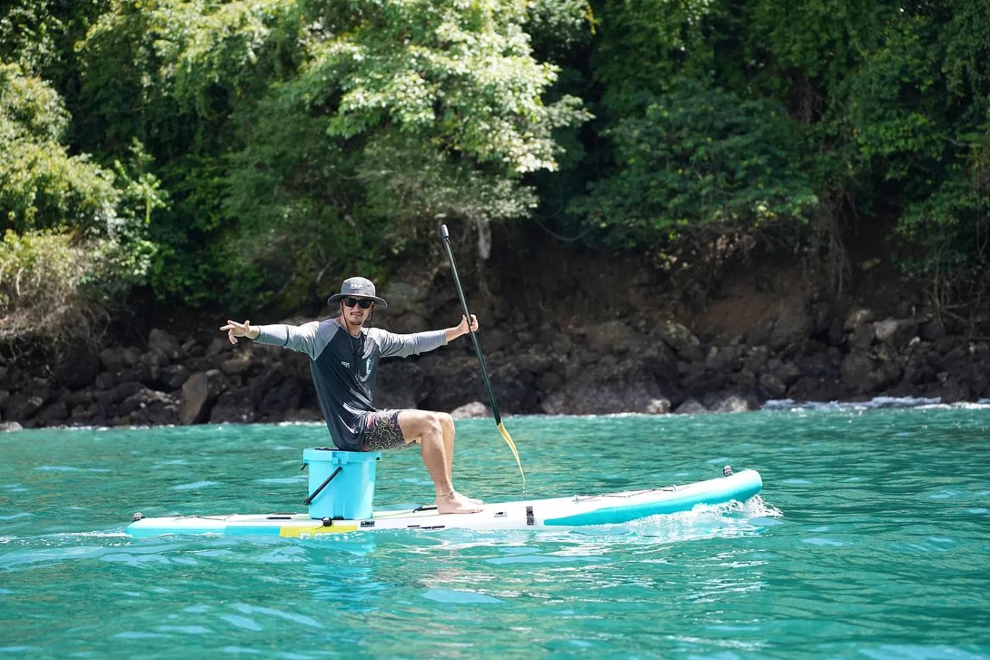 Paddleboarder standing on flat green water below the rainforest cliffs