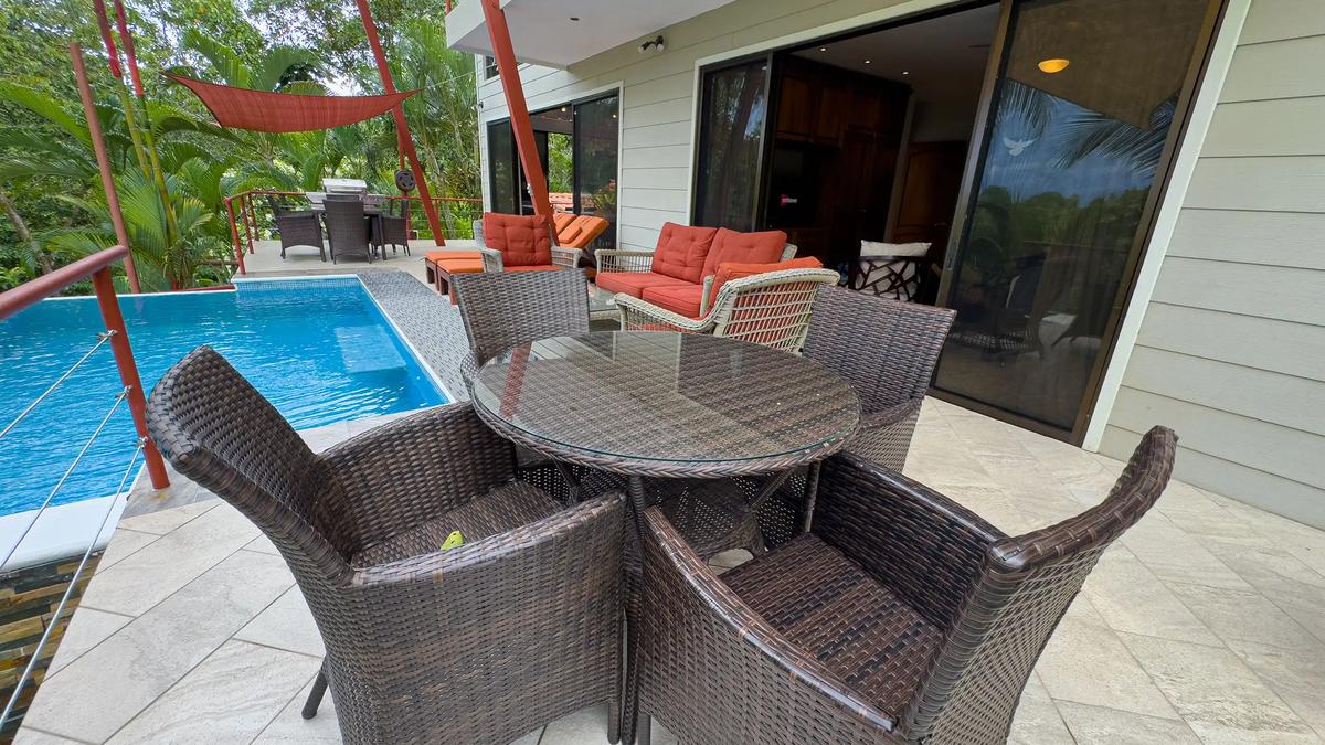 Poolside patio at Casa Serenidad with round wicker table and orange lounge cushions