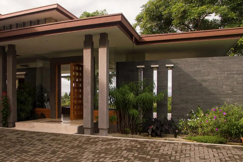 Covered front entrance of Casa Contee with stone wall and tropical plantings