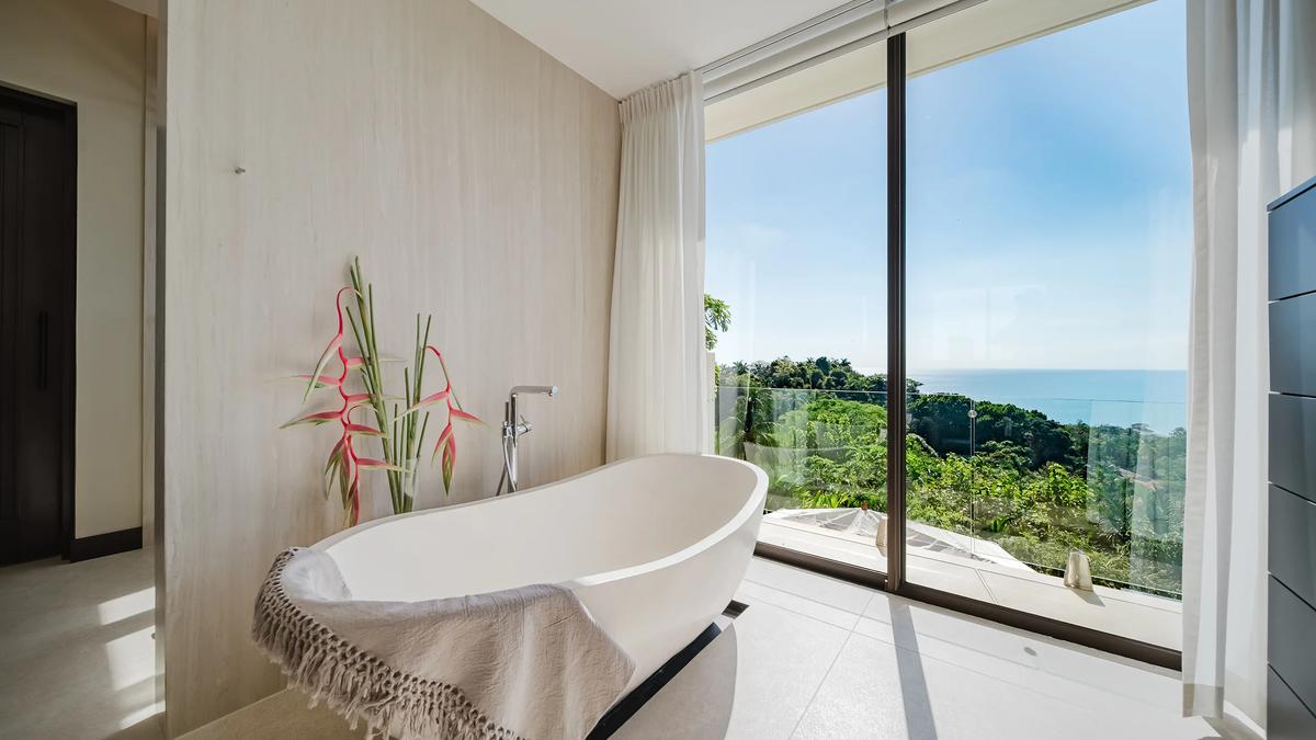 Freestanding bathtub at Casa Nola beside floor to ceiling glass and the ocean