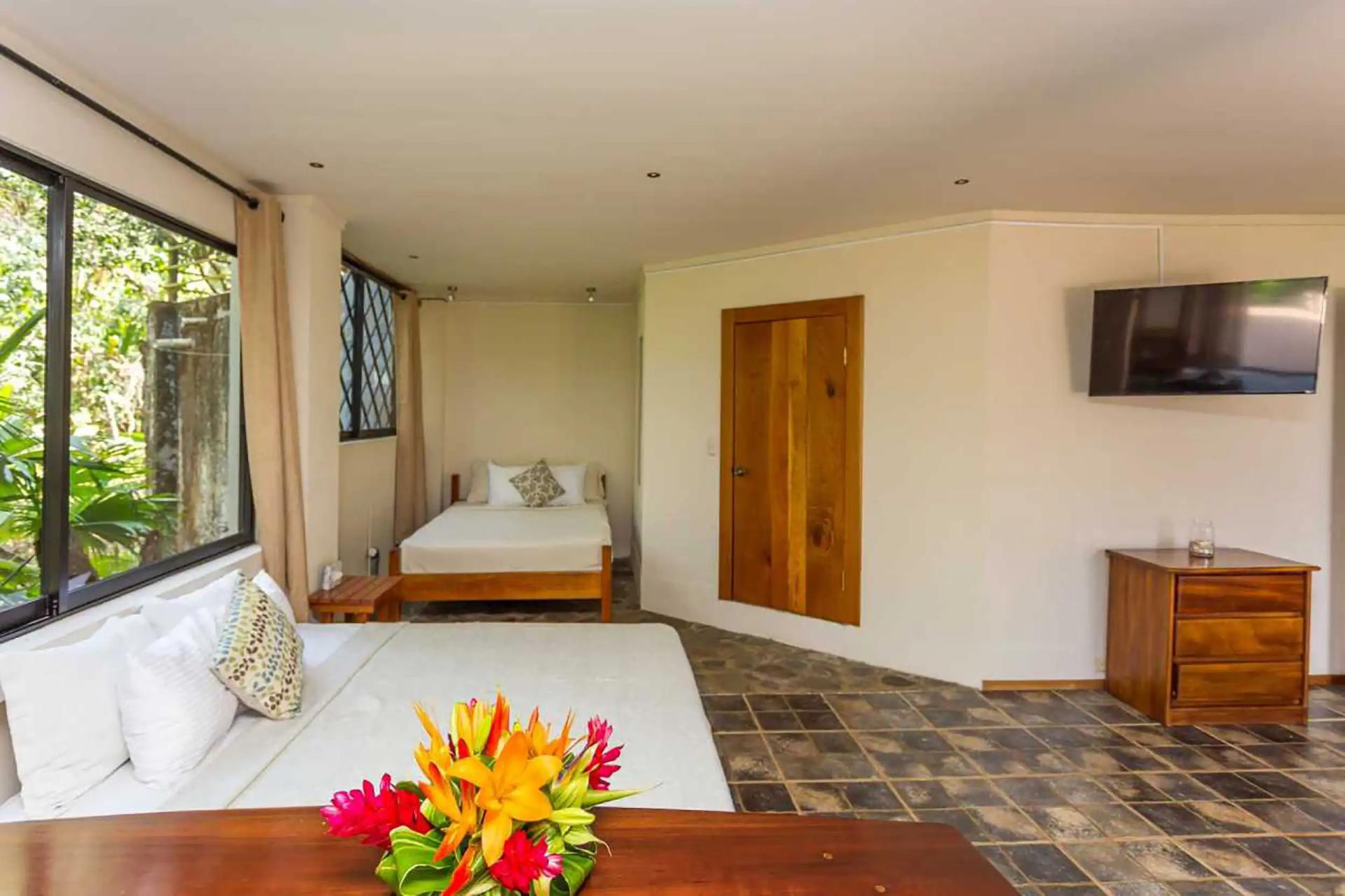 Casa Luz bedroom with two beds, wall mounted TV and tropical flowers